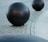 Large black spherical objects placed on a cobblestone surface, with a curved path of smooth stone tiles visible nearby. The setting appears to be outdoors.