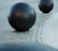 Large black spherical objects placed on a cobblestone surface, with a curved path of smooth stone tiles visible nearby. The setting appears to be outdoors.