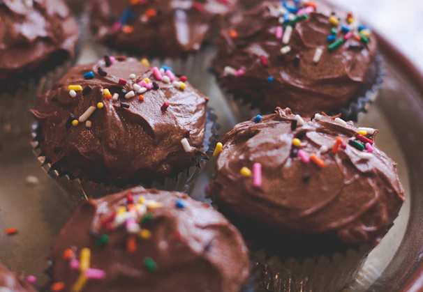 Close-up of rich chocolate cupcakes topped with glossy chocolate buttercream and gold sprinkles