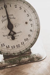 An old mechanical weighing scale with a rustic appearance. The dial has numbers from 0 to 23 and the text 'American Family Scale' printed on it. The base shows signs of wear with chipped paint and a greenish hue.