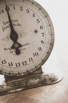 An old mechanical weighing scale with a rustic appearance. The dial has numbers from 0 to 23 and the text 'American Family Scale' printed on it. The base shows signs of wear with chipped paint and a greenish hue.