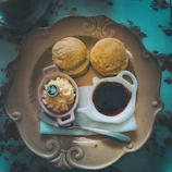 A steaming cup of freshly brewed tea beside a warm scone topped with clotted cream and jam.