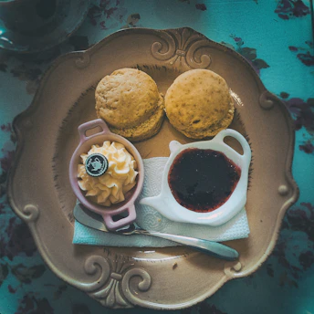 A delicate china teapot with cups, scones with jam and cream on a vintage plate