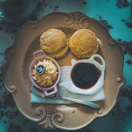 A cozy scene of a teacup beside a plate of buttery scones with clotted cream and jam.