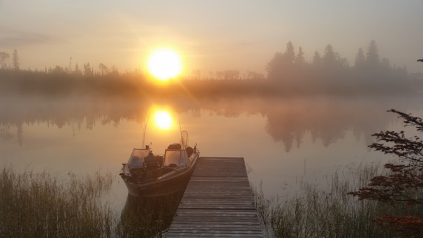 A serene lakeside scene at dawn, with gentle ripples on the water and a lone boat tied to a wooden dock.