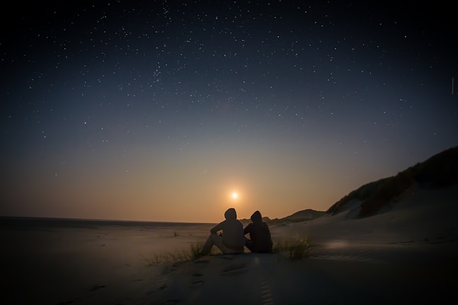 silhouette of two person sitting during golden hour