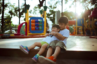 boy carrying child while sitting on gray concrete platform