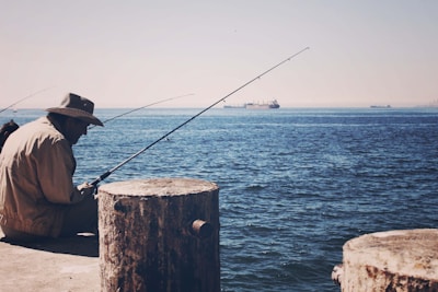 A close-up of a rugged trucker hat resting on a wooden dock with a fishing rod and calm water in the background.