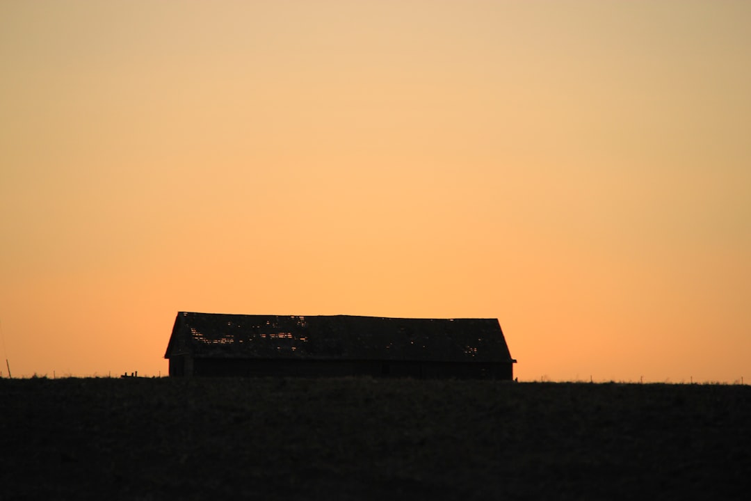 silhouette of house on grass field during sunset