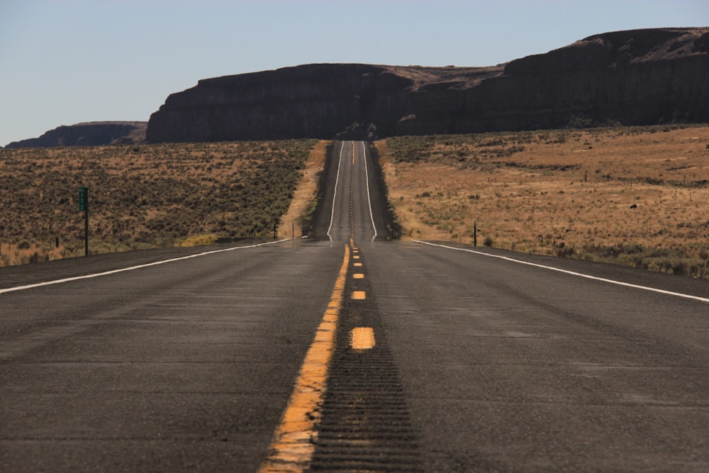 gray asphalt road between brown grass field during daytime