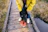 A cheerful man walking his small dog wearing bright yellow rain boots on a rainy city sidewalk.