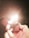 A hand is holding a metal lighter that is lit, emitting a bright flame. The background is dark, enhancing the glow of the flame, which casts reflections on the lighter's surface.