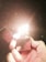 A hand is holding a metal lighter that is lit, emitting a bright flame. The background is dark, enhancing the glow of the flame, which casts reflections on the lighter's surface.