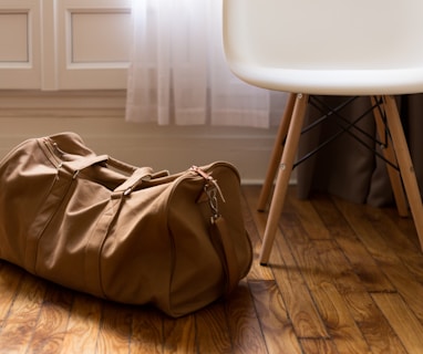 brown duffel bag beside white and brown wooden chair