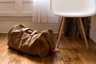 A sleek premium trolley bag standing upright on a polished wooden floor with soft natural light highlighting its rich leather texture.