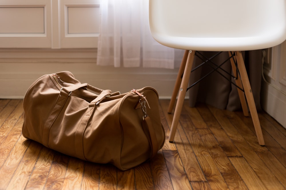 bolsa de lona marrón junto a una silla de madera blanca y marrón