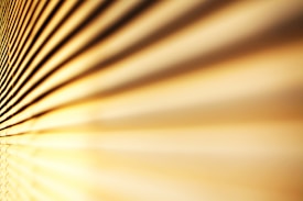 An abstract view of horizontal blinds with sunlight casting lines and shadows, creating a warm and textured pattern.