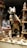 A taxidermy fox is posed upright with a rifle and a pheasant in its hands. Surrounding the fox are various decorative items, including beer steins with Bavarian designs, glass mugs, and ornate metal objects. The scene resembles an eclectic display of rustic and hunting-themed memorabilia with a playful twist.