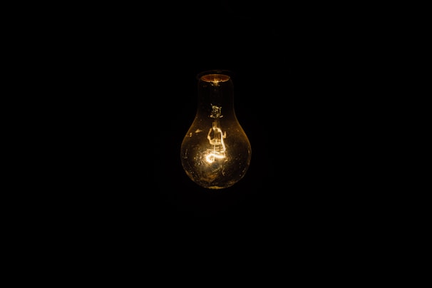 A minimalist photo of a single illuminated light bulb hanging in darkness.