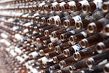 A large number of empty brown glass bottles are arranged in a dense, organized pattern. The bottles are positioned horizontally, with their necks facing outward. Some labels are still visible on the bottles.