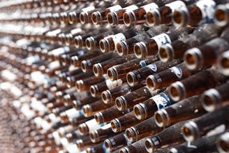 A large number of empty brown glass bottles are arranged in a dense, organized pattern. The bottles are positioned horizontally, with their necks facing outward. Some labels are still visible on the bottles.