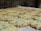 A batch of freshly baked chocolate chip cookies is spread out on a baking sheet. The cookies have a golden-brown color with visible chocolate chips throughout.