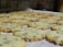 A batch of freshly baked chocolate chip cookies is spread out on a baking sheet. The cookies have a golden-brown color with visible chocolate chips throughout.