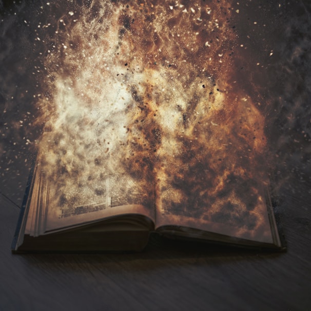 An open book appears to be engulfed in swirling flames, with sparks and smoke surrounding it. The intense fiery effect creates a dramatic and surreal scene, suggesting destruction or transformation.