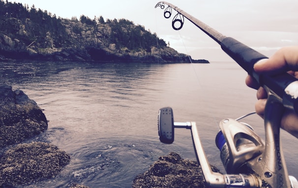 person fishing using black and silver fishing rod during daytime