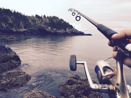 person fishing using black and silver fishing rod during daytime in East Sooke Park Canada