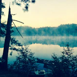 A serene moment capturing a traveler reflecting by a calm lake at dawn.