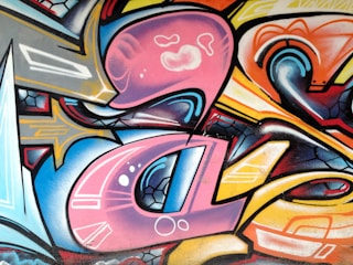 Vibrant and dynamic graffiti artwork featuring a mix of abstract shapes and flowing lines in a variety of bold colors. The composition includes curved forms and sharp edges, blending different patterns and textures seamlessly.