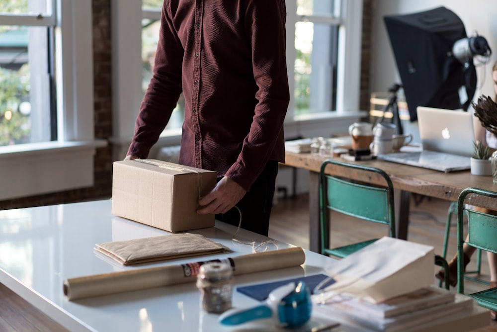 Persona sosteniendo una caja de cartón sobre la mesa