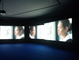 Multiple screens display the image of a woman looking out a window, each screen showing a slightly different angle or close-up. She appears deep in thought, with light illuminating her face.