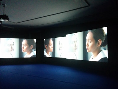 Multiple screens display the image of a woman looking out a window, each screen showing a slightly different angle or close-up. She appears deep in thought, with light illuminating her face.