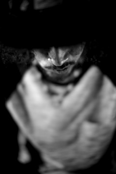 A blurred, monochromatic image focusing on the upper part of a person's face, partially obscured by a shadow, creating a mysterious atmosphere. The details are intentionally unclear, adding an element of intrigue.