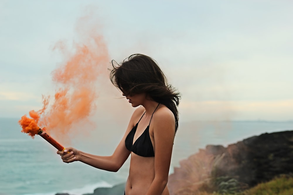 Mujer en bikini negro sosteniendo humo naranja