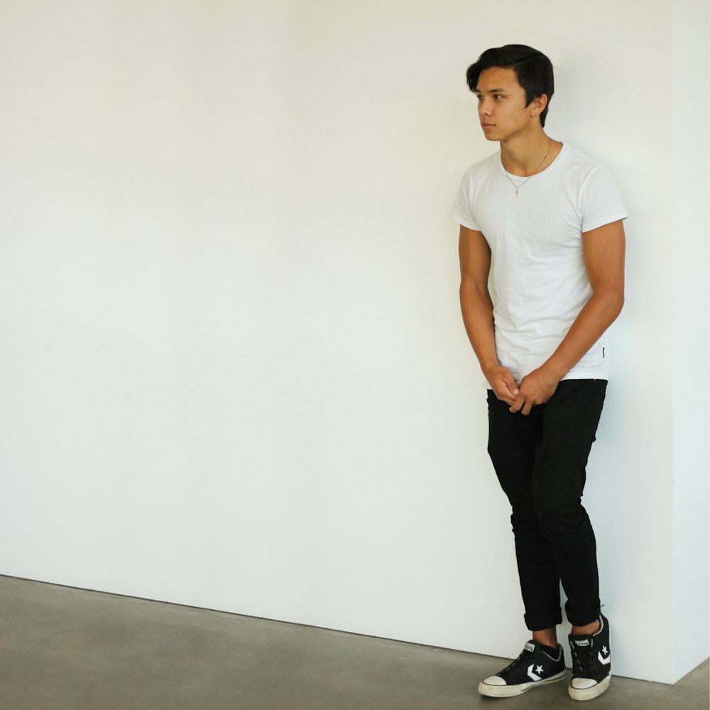 man wearing white t-shirt and black jeans standing near white wall