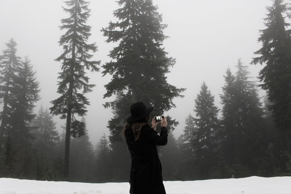 woman takes photo at the snowfield surrounded with trees