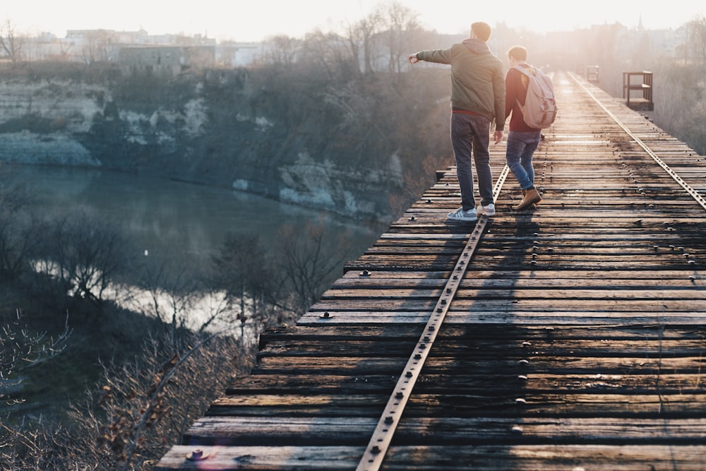 two boy standing on brown train track bridge near river