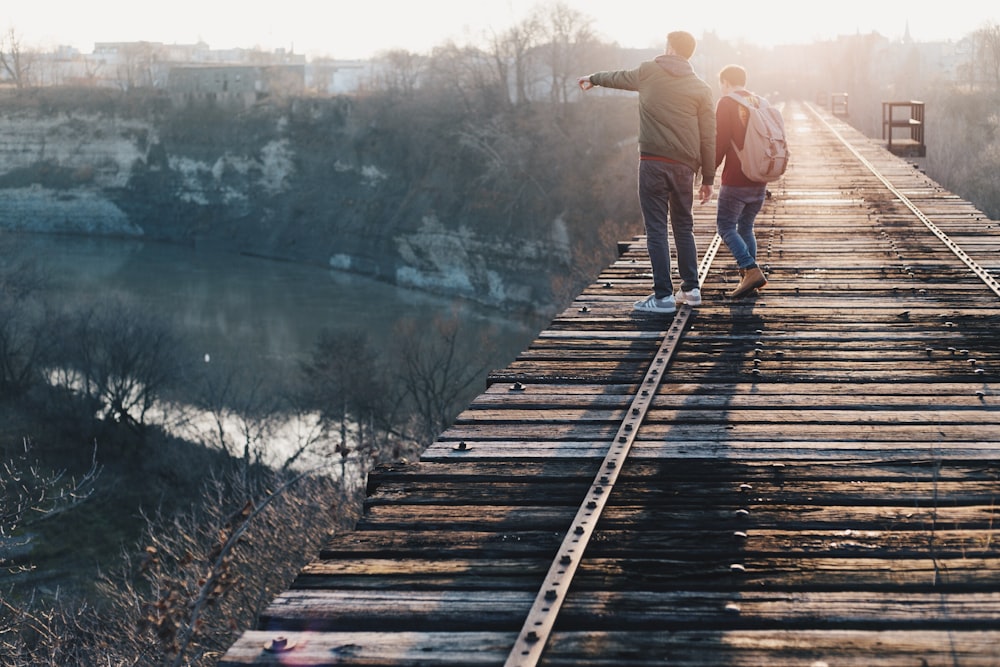 Dos muchachos de pie en el puente de la vía del tren marrón cerca del río