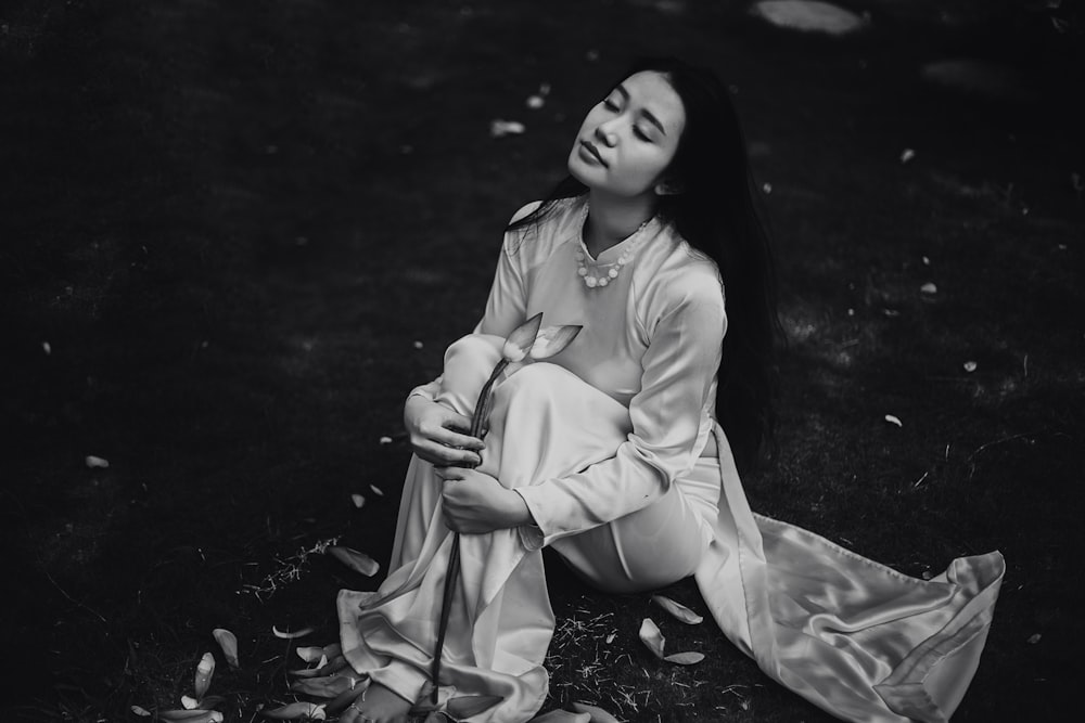 woman wearing white dress sitting on ground grayscale photo