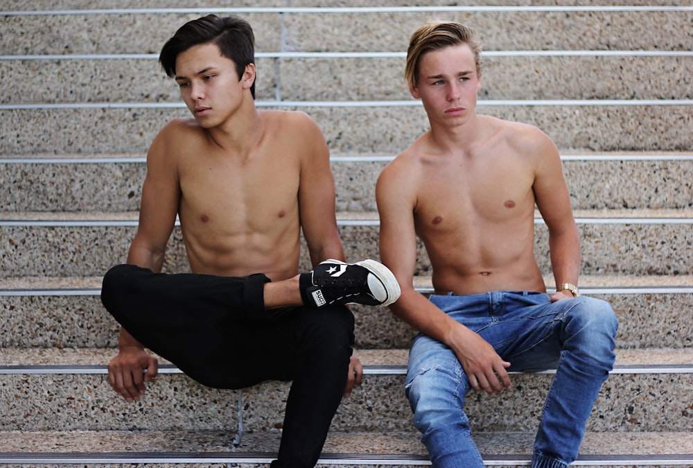 zwei Oben-ohne-Männer in Jeans sitzen auf einer Treppe