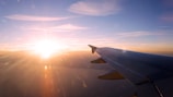 A sunrise view from an airplane window showing clouds glowing orange