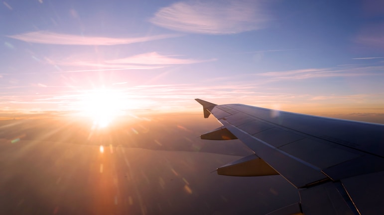 A sunrise view from an airplane window showing clouds glowing orange