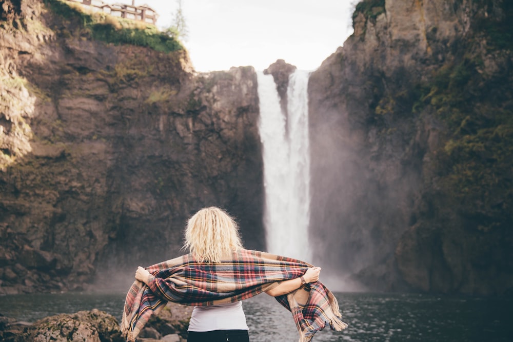 woman standing on stone beside the waterfalls