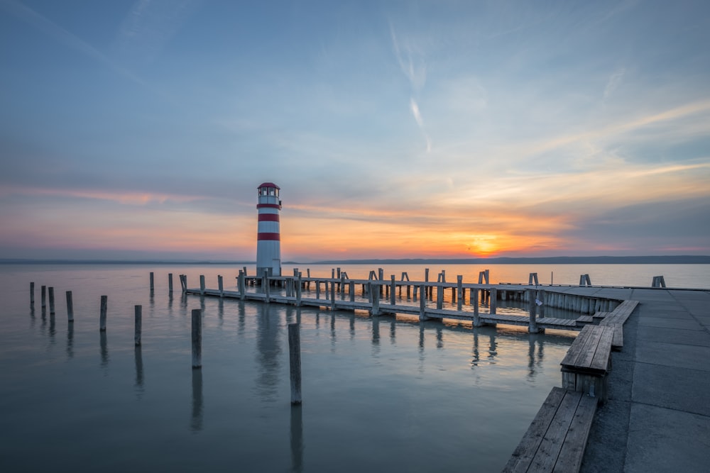 lighthouse at end of docks under clear sky during sunrise