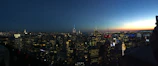 A panoramic view of a city skyline highlighting illuminated skyscrapers at dusk.