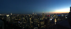 A panoramic view of a city skyline highlighting illuminated skyscrapers at dusk.
