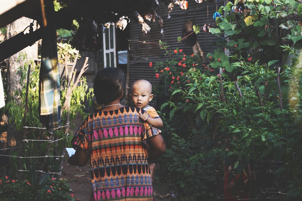 woman carrying child near green leafed plants